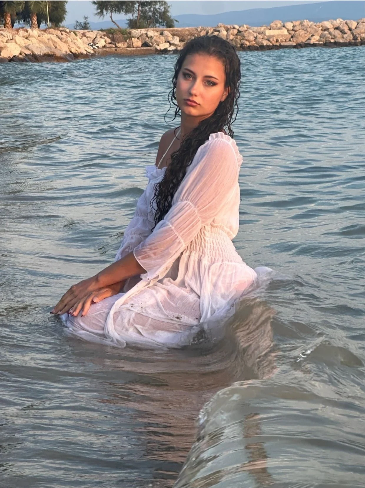 Samia Winkler kneeling in the sea in a white dress, looking at the camera